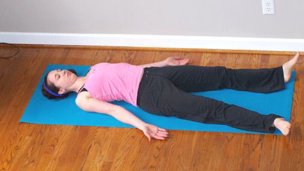 mujer realizando la postura del cadáver durante una práctica de yoga
