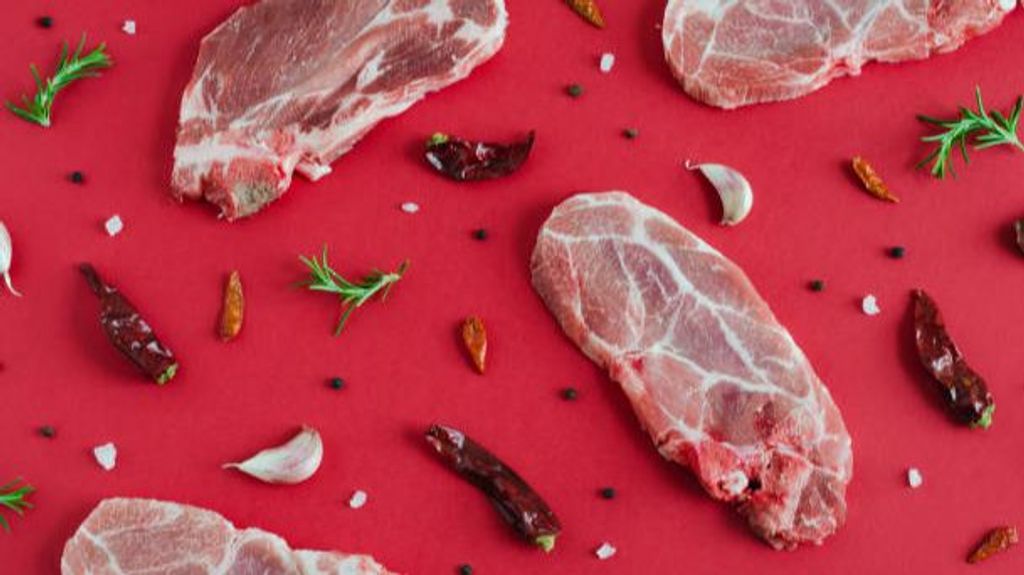 Raw pork steaks with spices on red background. Flat lay.