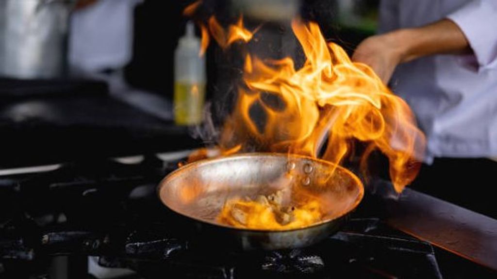 Close-up on a chef flaming food on a pan at a restaurant's kitchen