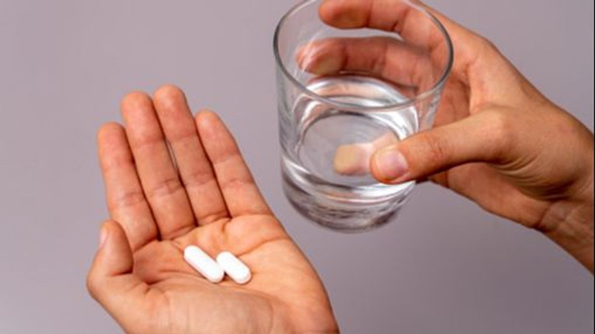 Elevated view of hand holding pills and a glass of water