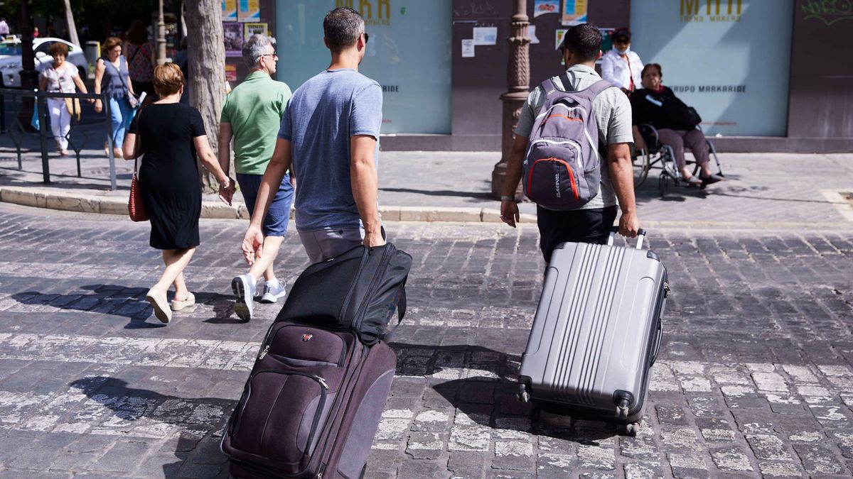 Dos turistas, con maletas, cruzan un paso de peatones a 21 de junio de 2022 en Sevilla (Andalucía, España)