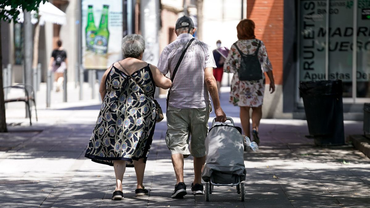 Una pareja de ancianos camina por la calle con un carro de compra, a 27 de julio de 2021, en Madrid,
