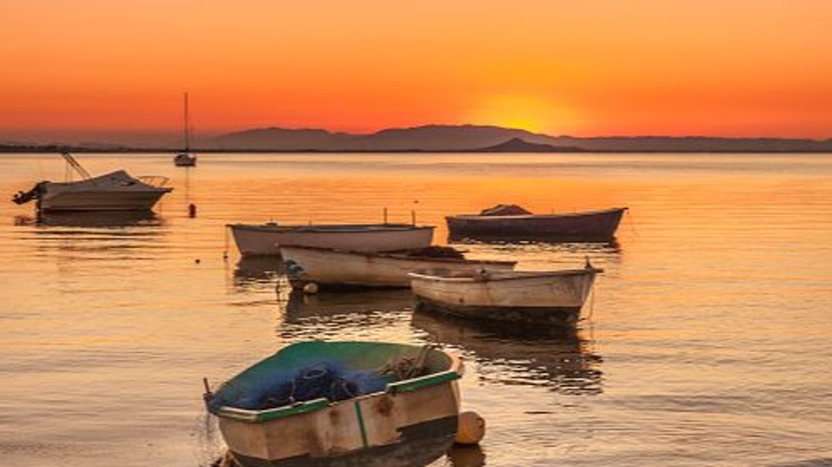 Abandoned boats and others for recreation and fishing in line in the Mar Menor, a salt water lake. The boats follow the direction of the sunset on the horizon