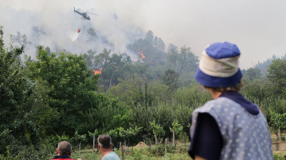 Una mujer mirando cómo un helicóptero actúa contra las llamas en O Courel (Lugo).