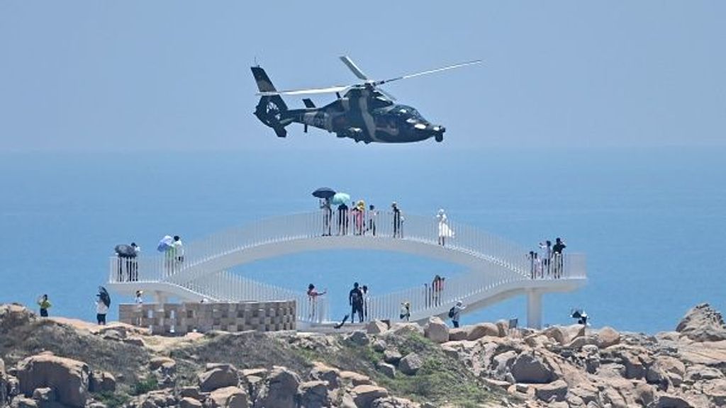 TOPSHOT - Tourists look on as a Chinese military helicopter flies past Pingtan island, one of mainland China's closest point from Taiwan, in Fujian province on August 4, 2022, ahead of massive military drills off Taiwan following US House Speaker Nancy Pelosi's visit to the self-ruled island. - China is due on August 4 to kick off its largest-ever military exercises encircling Taiwan, in a show of force straddling vital international shipping lanes following a visit to the self-ruled island by US House Speaker Nancy Pelosi. (Photo by Hector RETAMAL / AFP) (Photo by HECTOR RETAMAL/AFP via Getty Images)