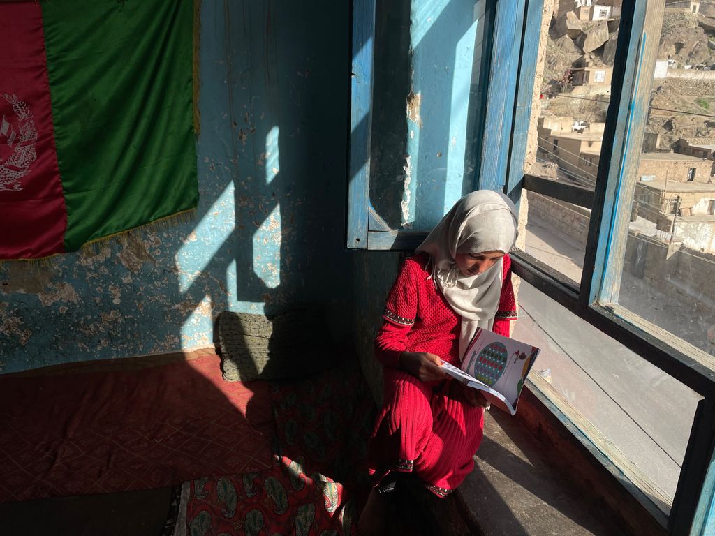 Yazin Harin de 13 años, lee un libro, apoyada en la ventana, desde la que vislumbra la mezquita.