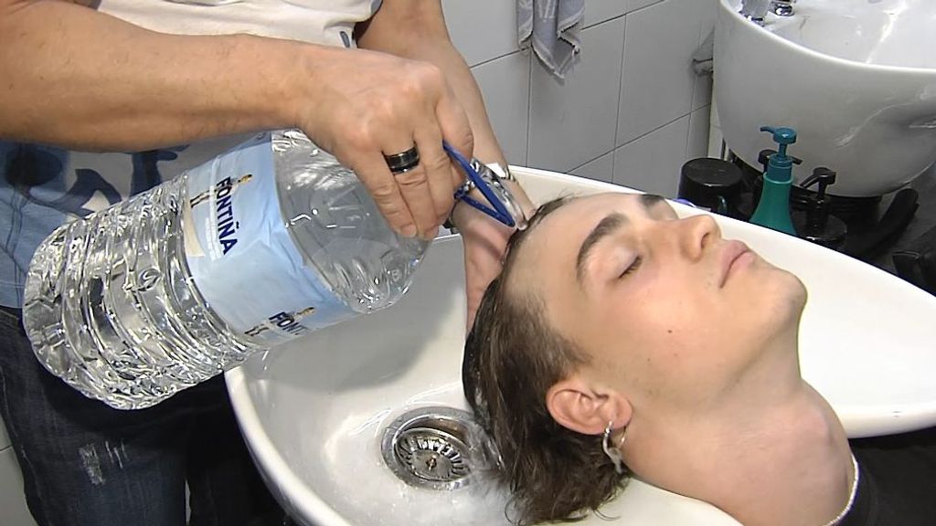 Un peluquero lava la cabeza a un cliente con una garrafa de agua.