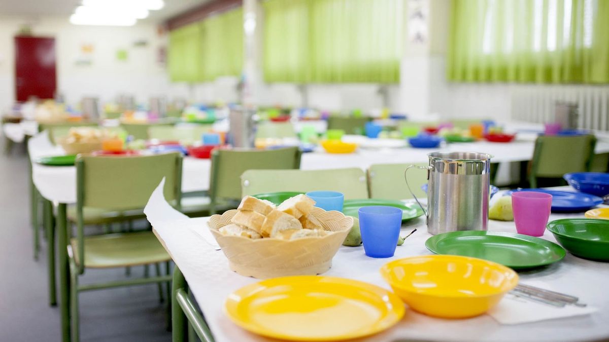 School dining room tables prepared for children to eat with glasses, plates, jugs.