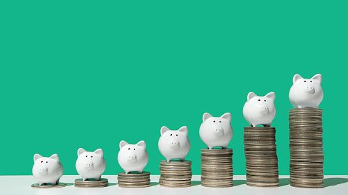 Little white piggy banks standing on top of 7 stacks of coins in ascending order on white surface, green background