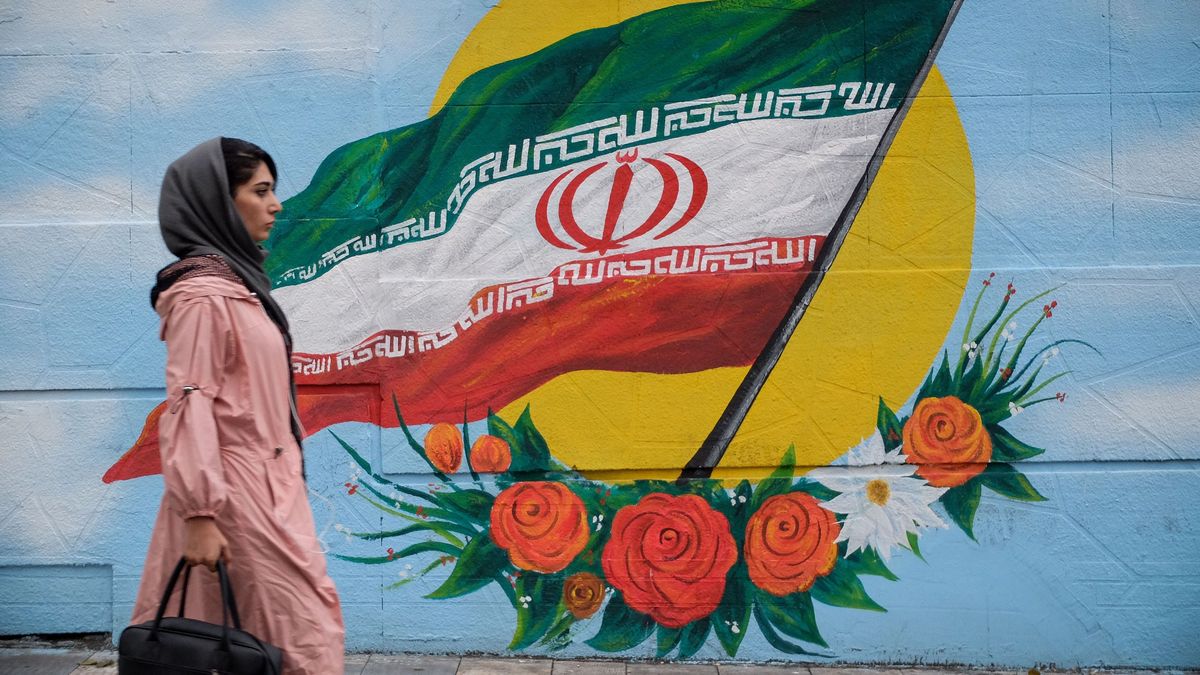 Una mujer camina frente a un mural con la bandera de Irán situado en una de las calles de Teherán