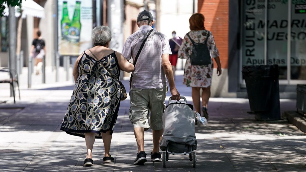 Una pareja de ancianos camina por la calle con un carro de compra