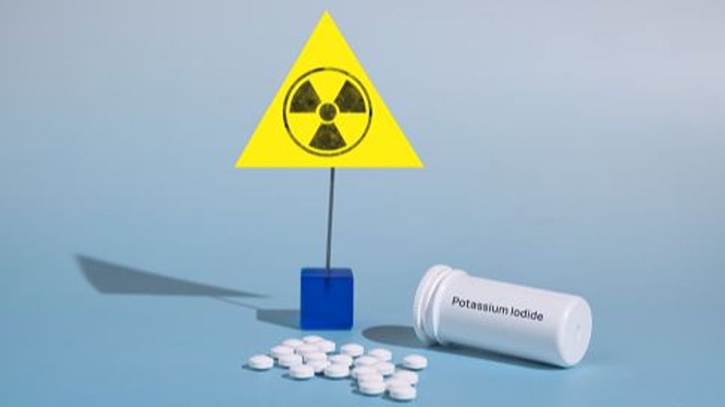 Potassium iodide tablets for use in case of radioactive contamination and radiation sign on a blue background. The name of the medicine is written on the box. Front view.
