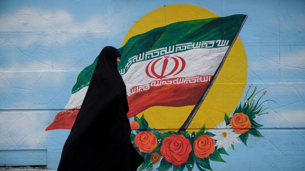 Una mujer con chador camina junto a un mural con la bandera de Irán en Teherán