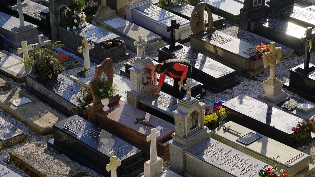 Archivo - Una mujer limpia una lápida del cementerio. Imagen de archivo.