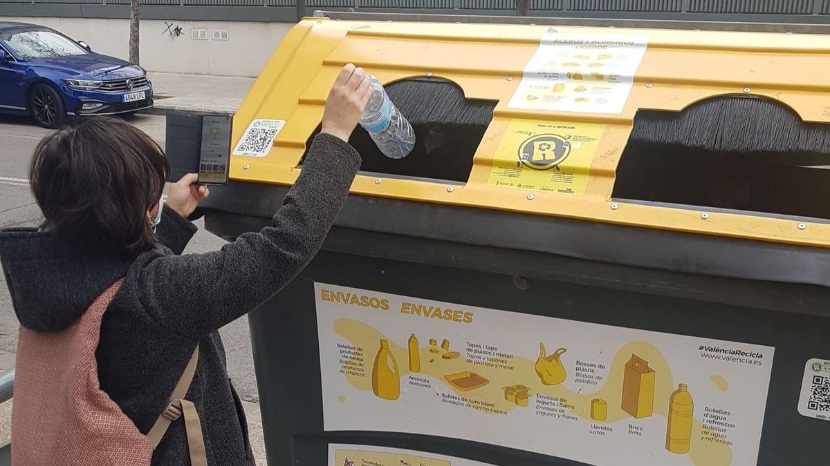 Una mujer deposita una botella de plástico en el contenedor amarillo