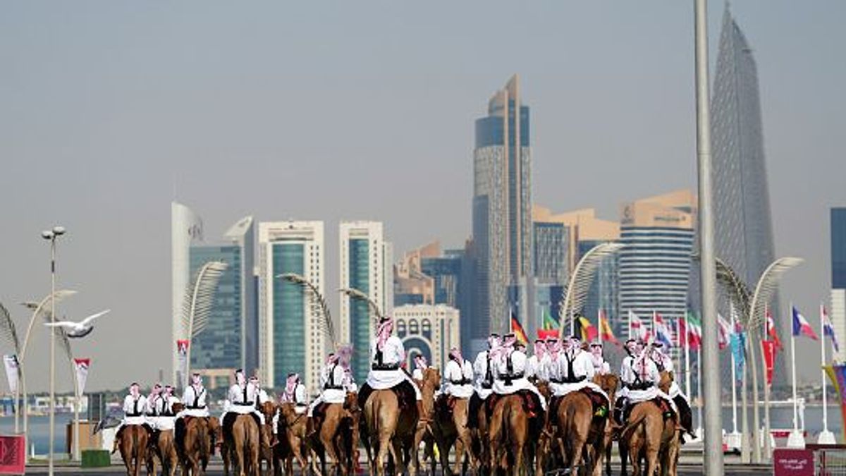 Camellos y jinetes durante un ejercicio matutino mientras ondean las banderas de las naciones competidoras antes de la Copa Mundial de la FIFA 2022 en Qatar