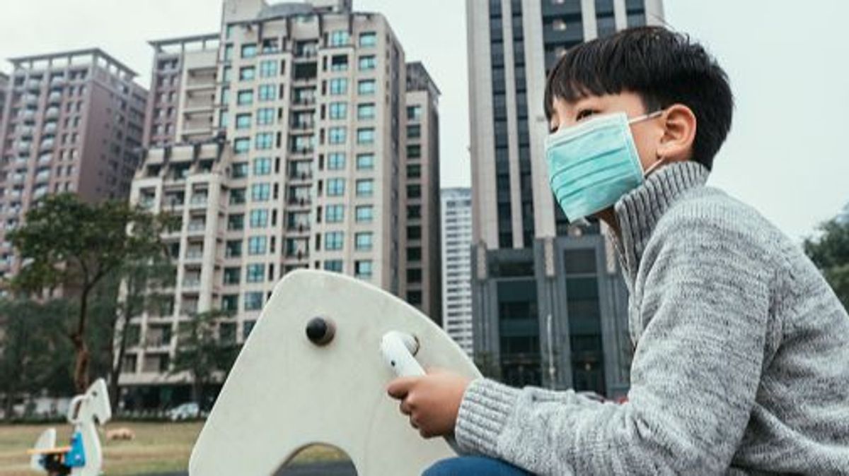 Asian boys play in the city playground, wearing masks against air pollution.
