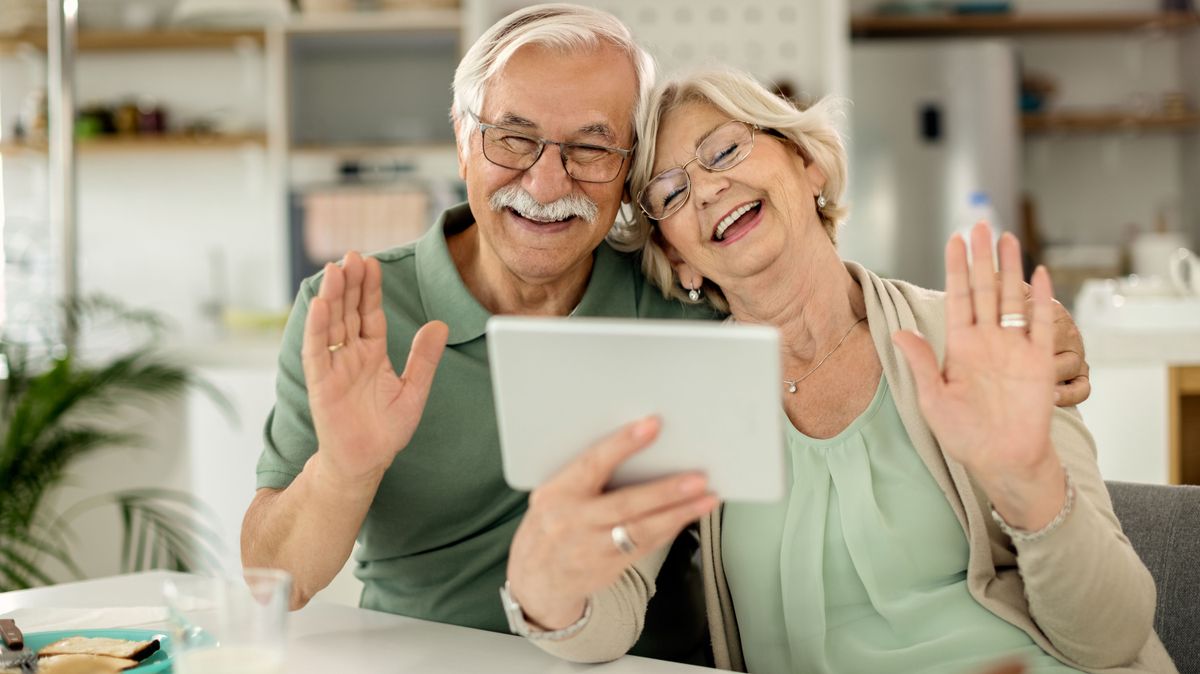 Cheerful mature couple waving during video call over touchpad.