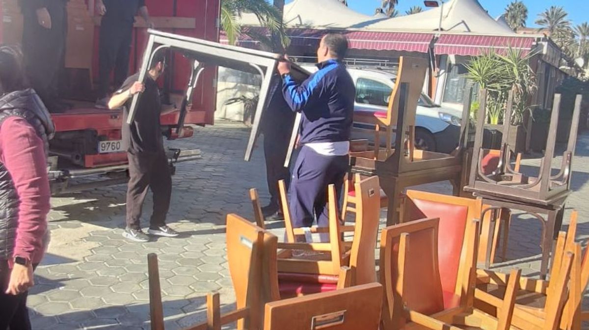 Operarios suben mesas de un restaurante de Port Olímpic al camión de mudanzas