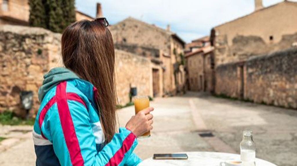 Young blonde woman drinking juice on a terrace of a bar in an old Spanish town.