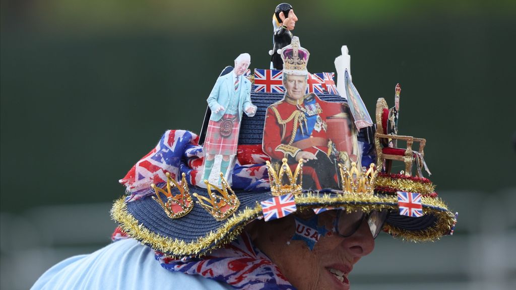 Una mujer luce un gorro personalizado con fotos y figuras de Carlos III por las calles de Londres mientras espera ver el momento de su coronación