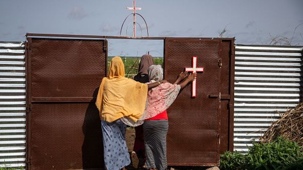 Tres mujeres tocan una cruz al salir de una iglesia católica en el campo de refugiados de Shagarab el 15 de agosto de 2021 en Shagarab, Sudán