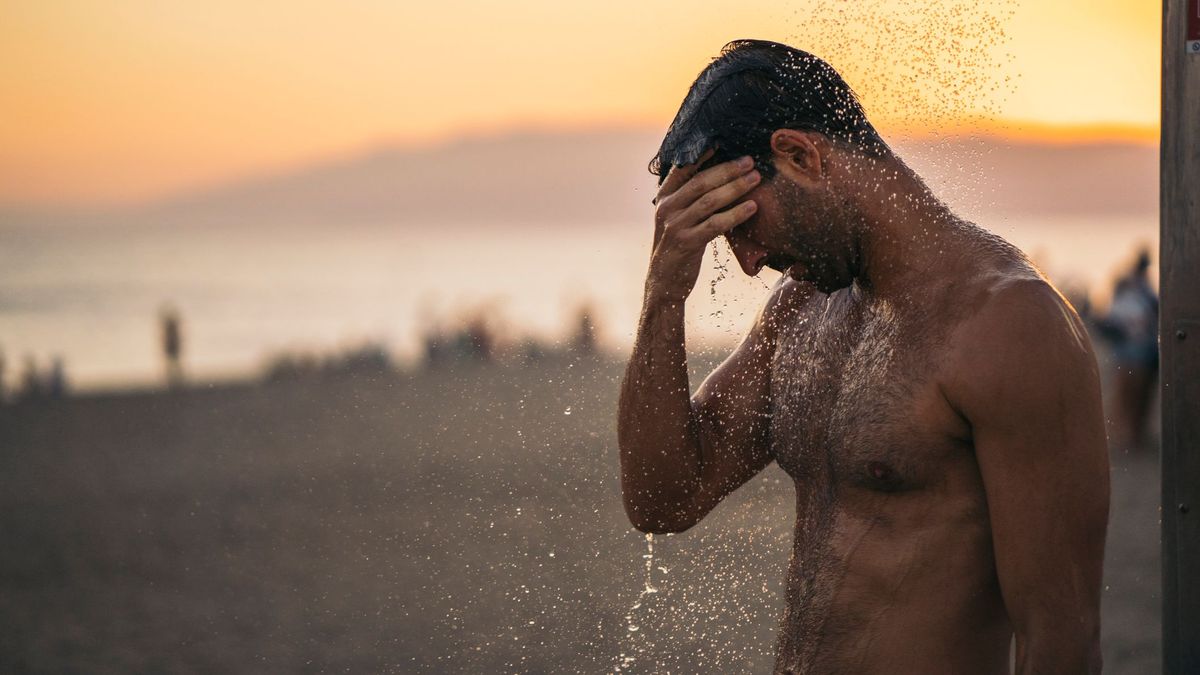 Un hombre se ducha en la playa tras un día de baño