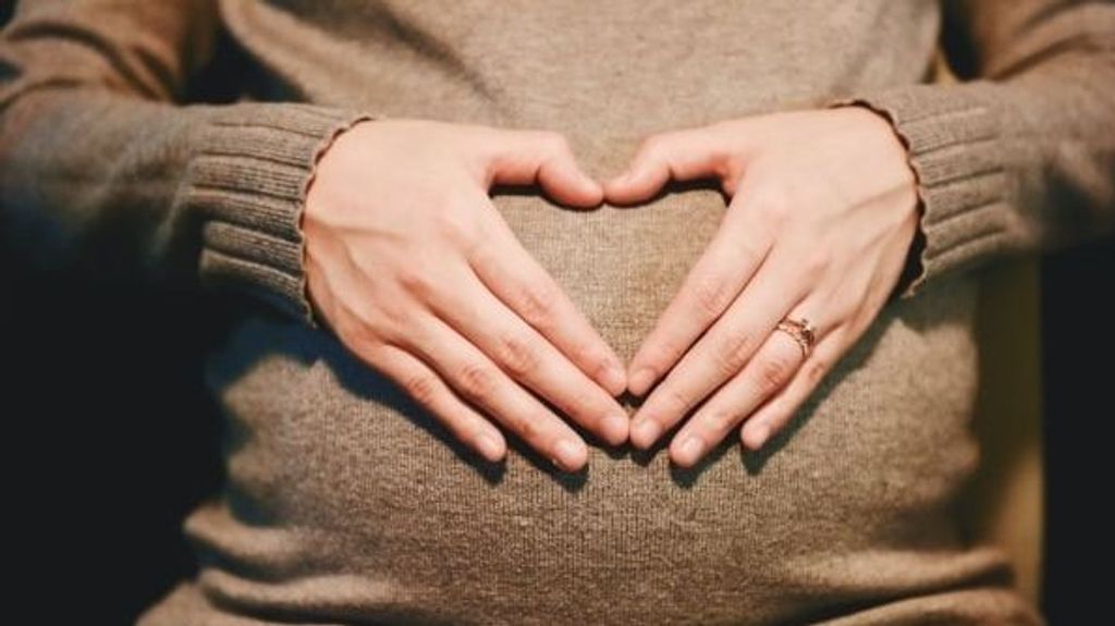 Una embarazada haciendo con su manos un corazón.