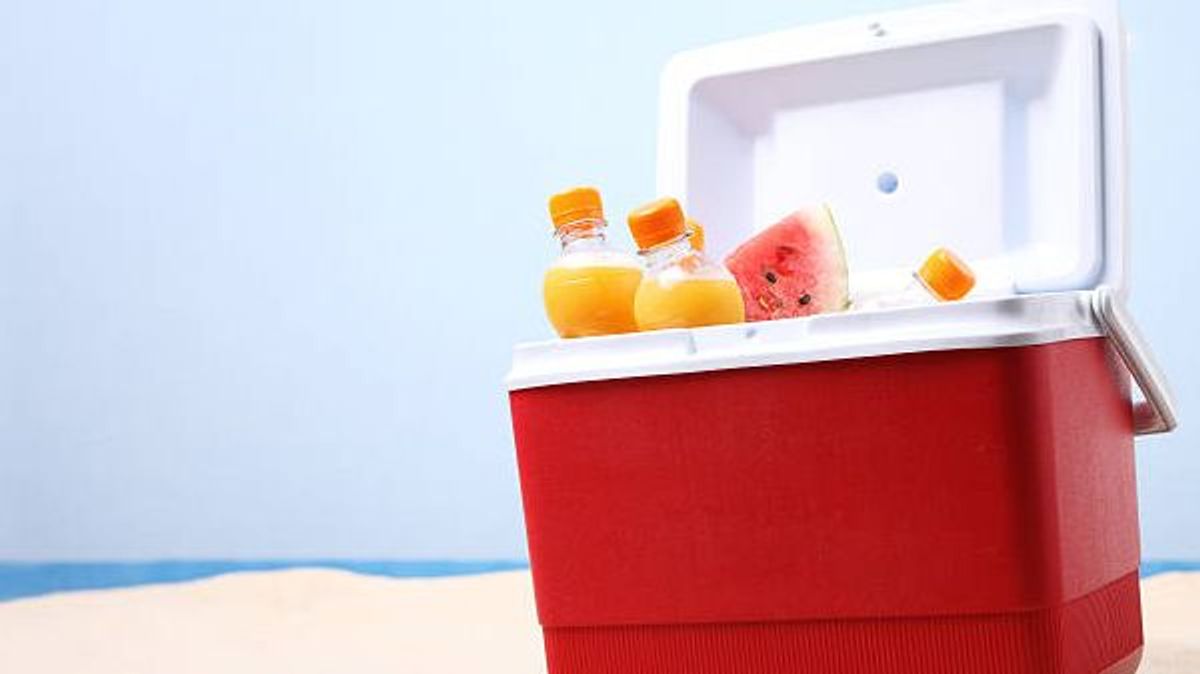 Open ice box with orange juice bottles on white sand at the beach.