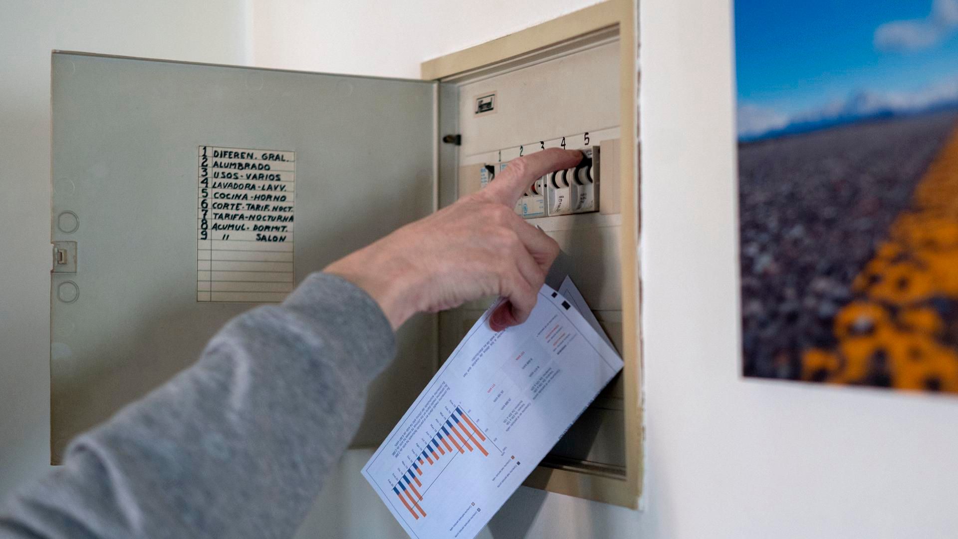 Archivo - Un hombre sube los plomos de la luz con una factura de luz en la mano, en Madrid (España).