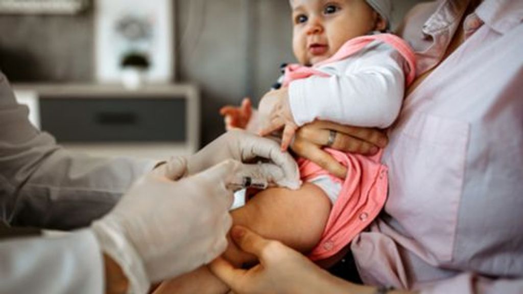 Pediatrician vaccinating a little baby girl while mother hold her in doctor's office