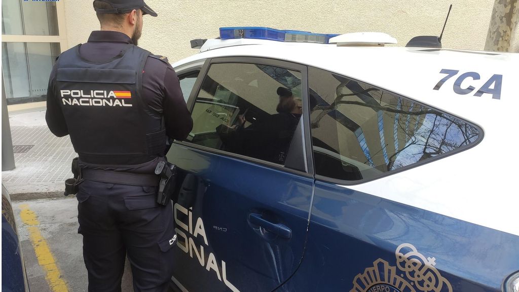 Archivo - Agente de la Policía Nacional de espaldas, junto a un coche patrulla.