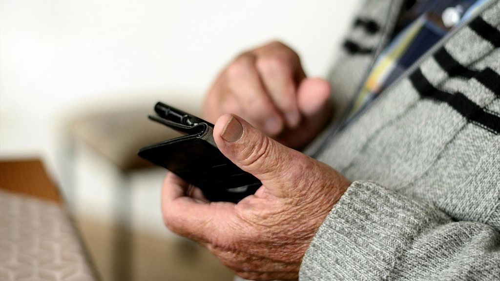 Archivo - Un pensionista con un teléfono móvil en la mano