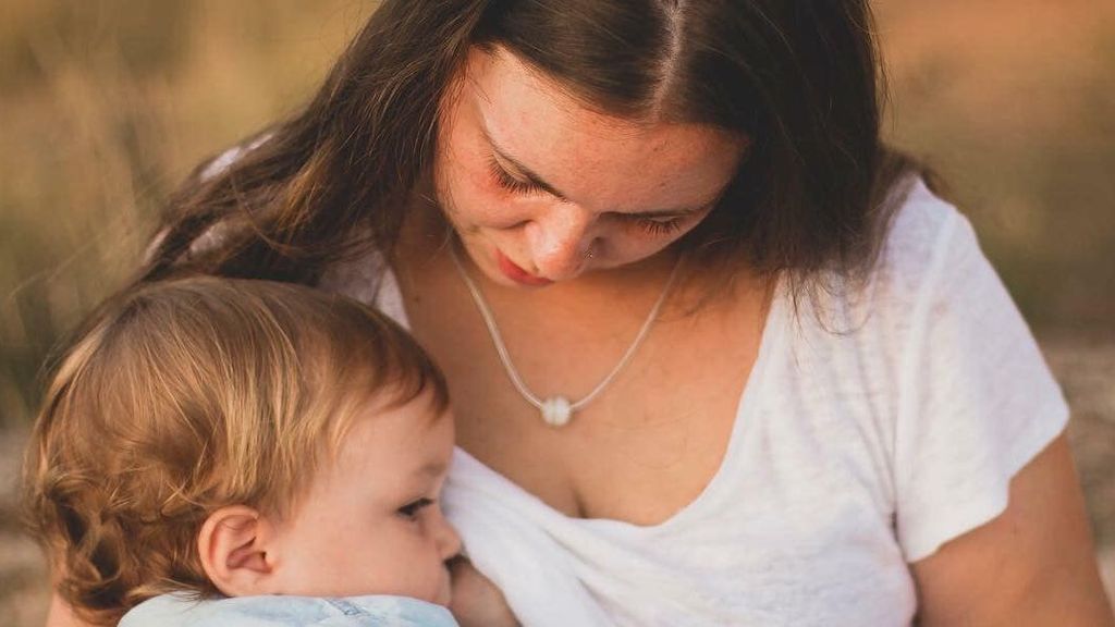 Una madre con un colgante da de mamar a su hijo