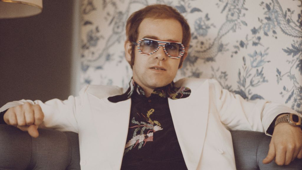 Elton John, con papel de pared psicodélico a su fondo