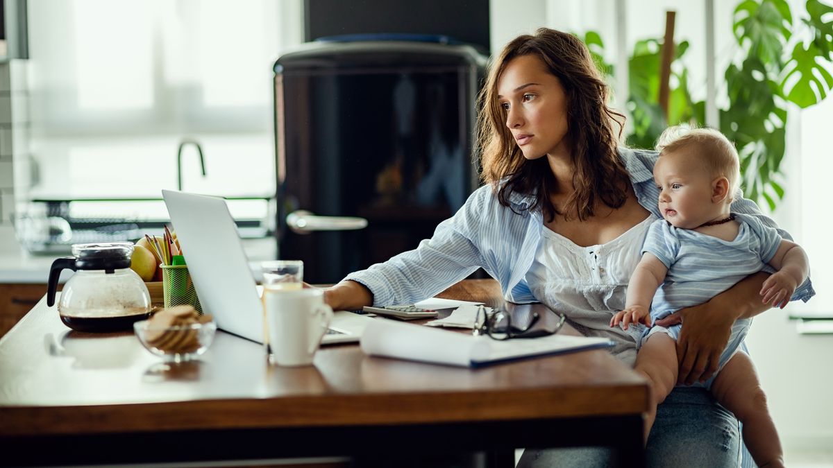 Young mother working on laptop while being with baby at home.