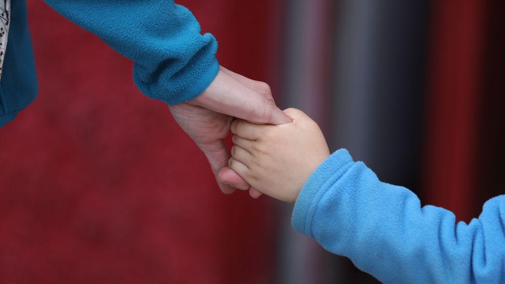 Un niño camina agarrado de la mano de una persona adulta