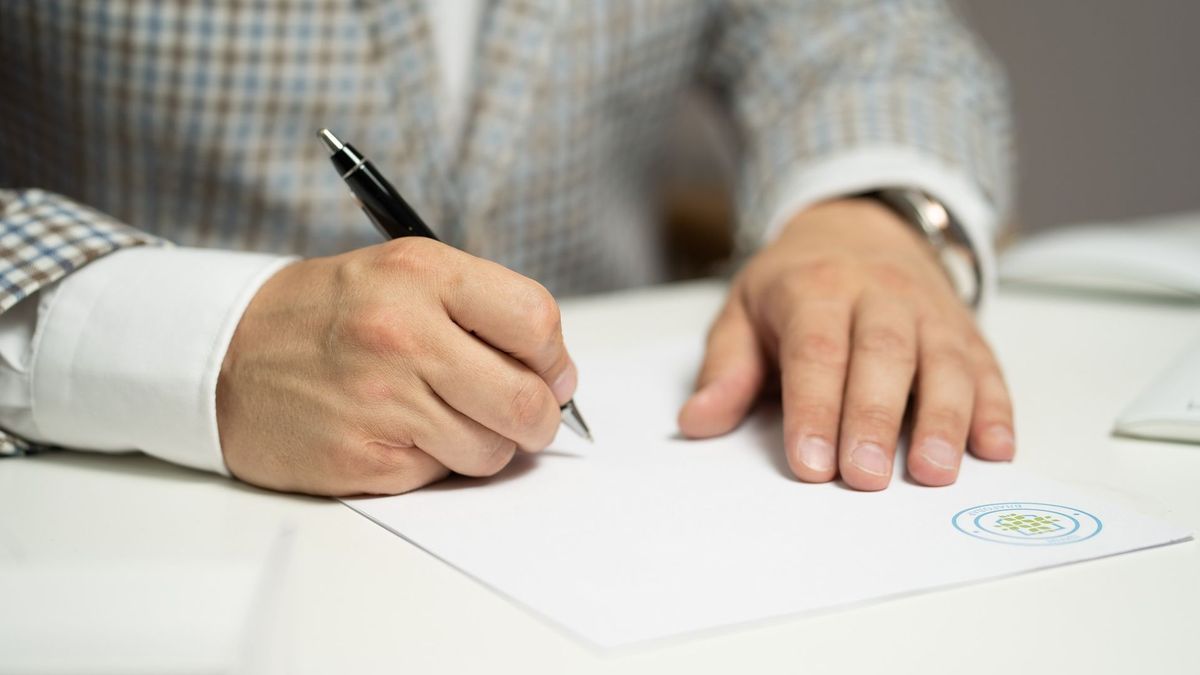 Hombre con un boli escribiendo en un documento sellado