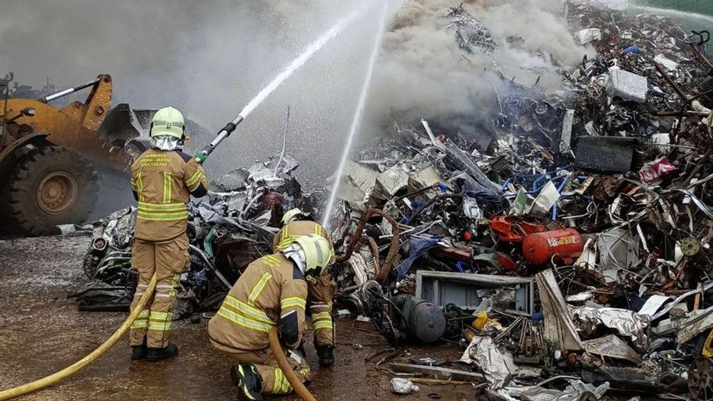 Efectivos de bombero tratan de apagar el fuego desatado en el montón de chatarra acumulado en el exterior de la empresa.