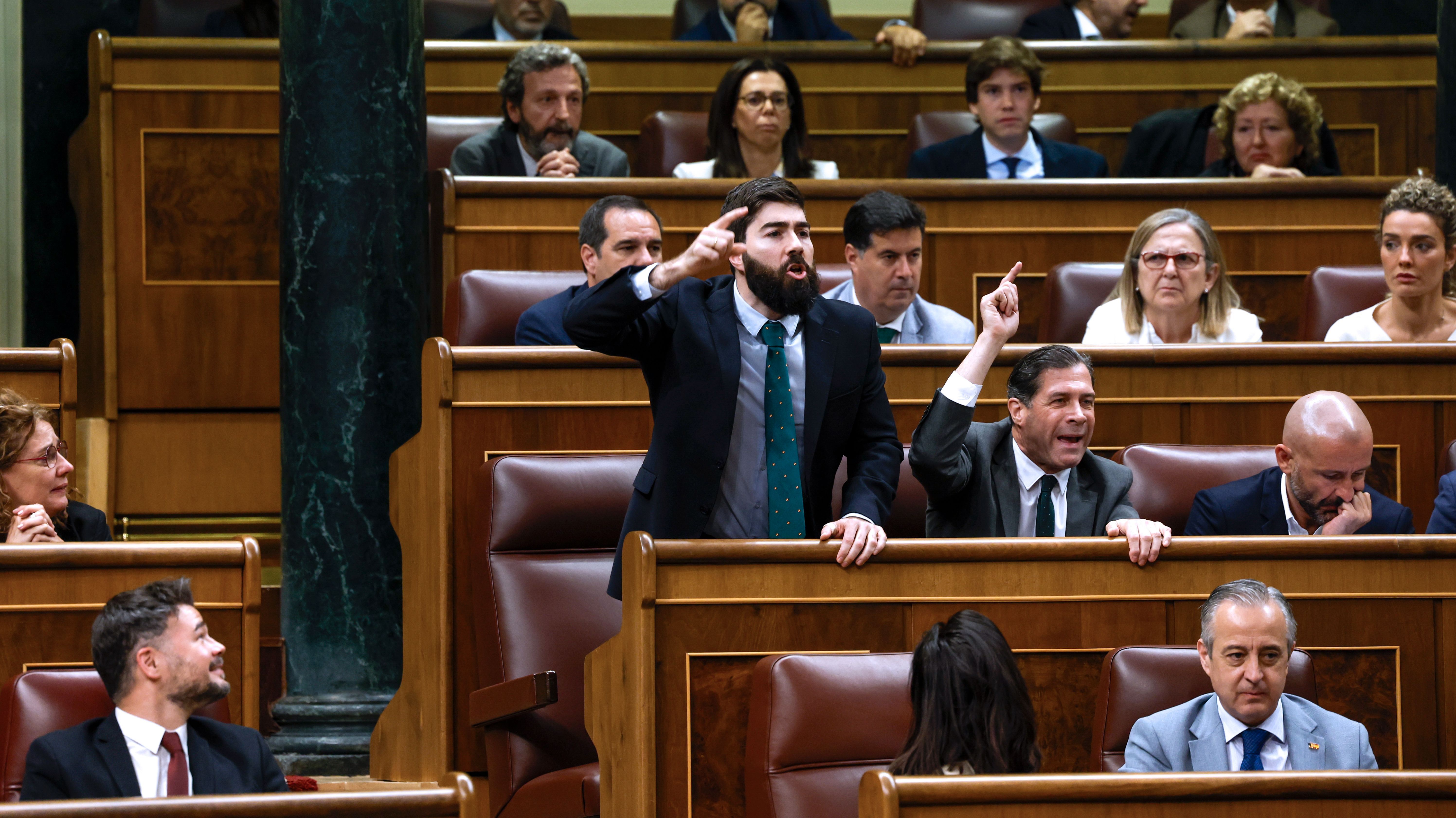 Los diputados de VOX Manuel Mariscal Zabala  y Pedro Fernández Hernández reaccionan tras la intervención del diputado de Sumar Gerardo Pisarello