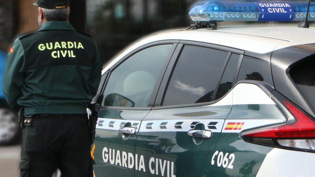 Archivo - Un agente de la Guardia Civil, de espaldas, de pie junto a un vehículo oficial.