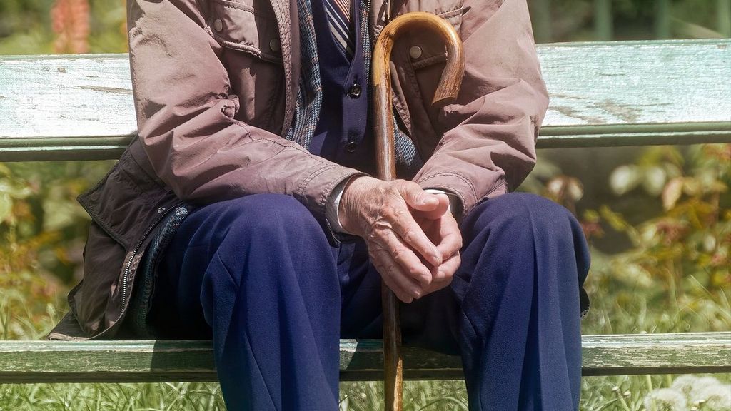 Anciano en soledad, con su garrote sentado en un banco