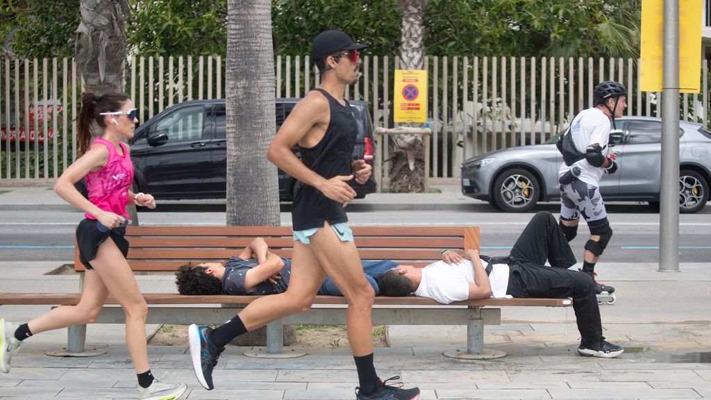 Dos personas duermen mientras otras practican ejercicio frente a la playa de la Barceloneta