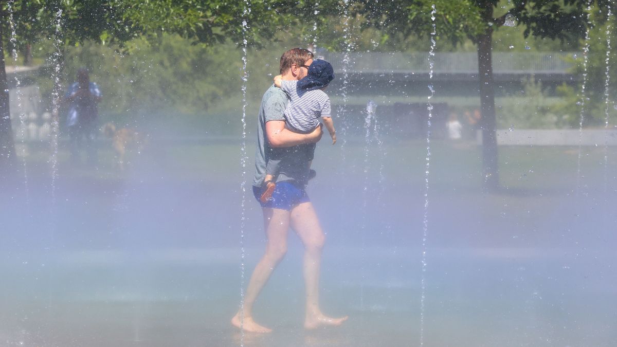 Un hombre con su hijo pasa por los chorros de agua de Madrid Río para combatir el calor