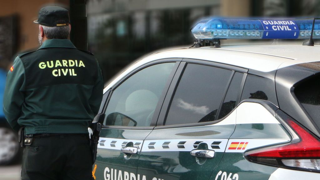 Un agente de la Guardia Civil, de espaldas, de pie junto a un vehículo oficial.