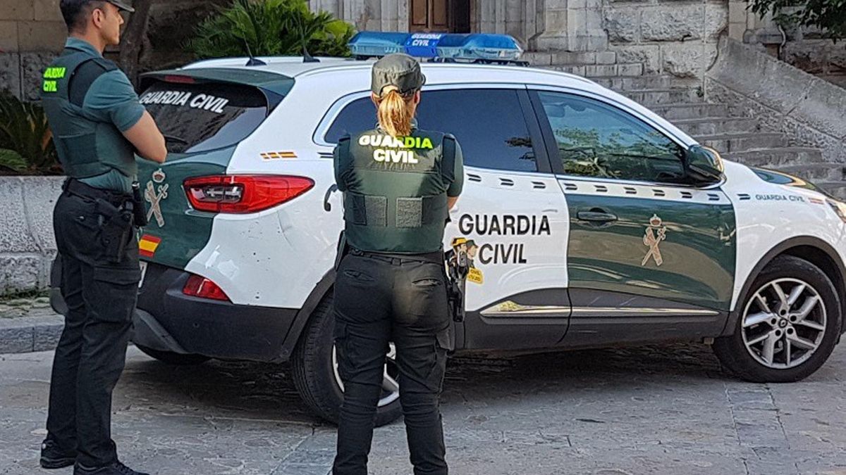 Archivo - Dos agentes de la Guardia Civil junto a un coche oficial.