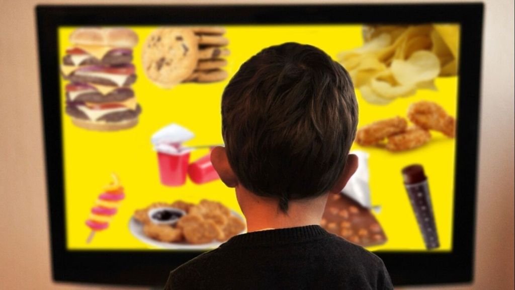 Un niño ve en la televisión un anuncio de comida no saludable