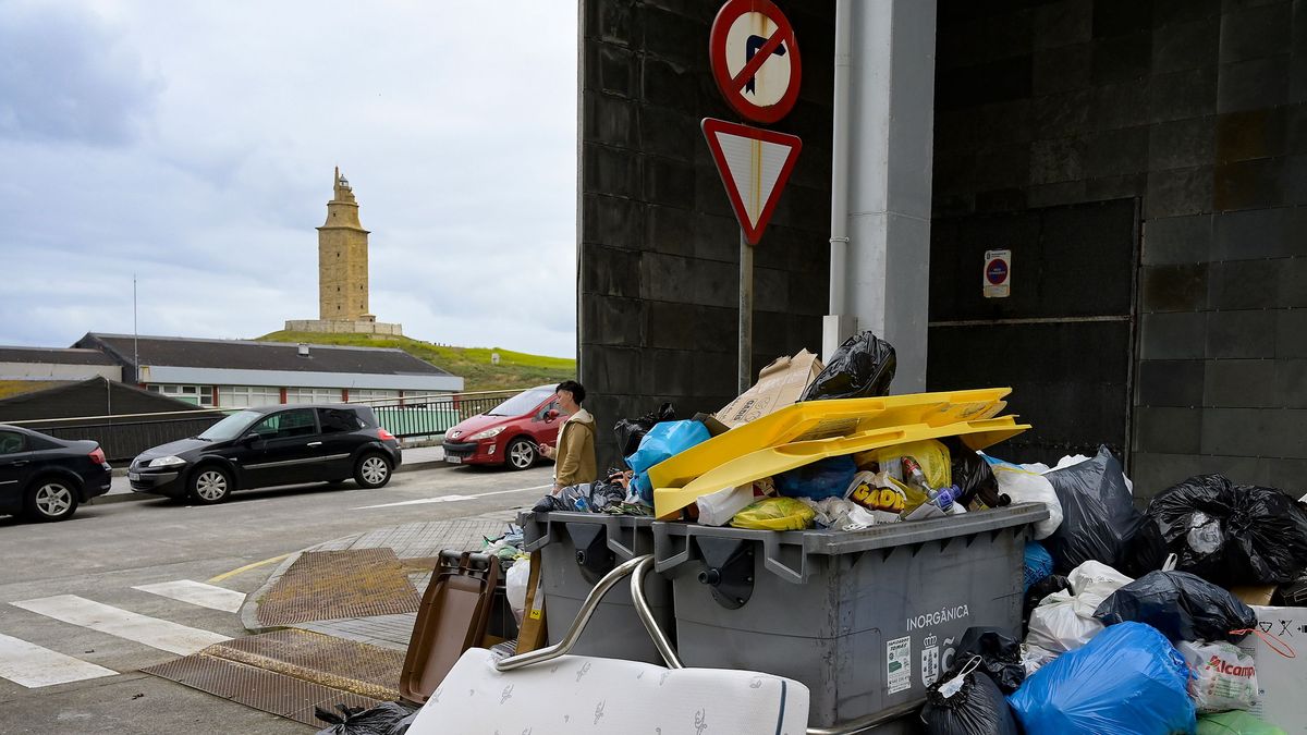 Contenedores rebosando de basura en el barrio de Monte Alto con la Torre de Hércules al fondo