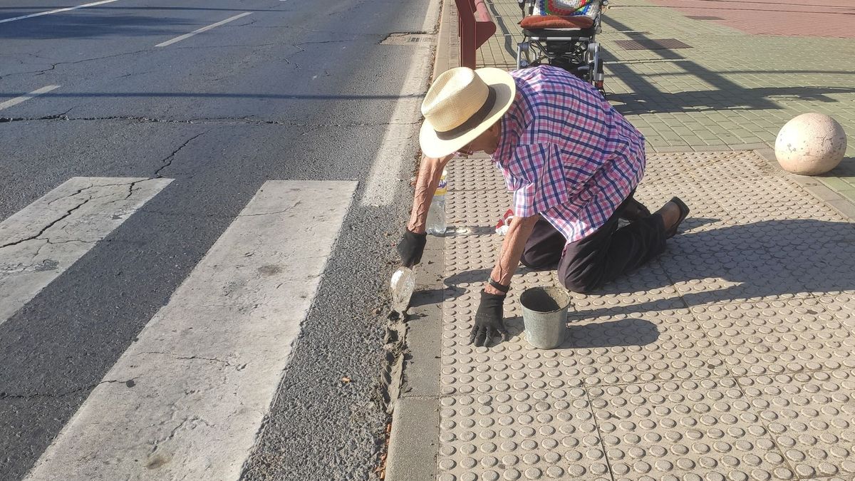 Un anciano rellena un bordillo para cruzar el paso de cebra en silla de ruedas en Aljaraque, Huelva