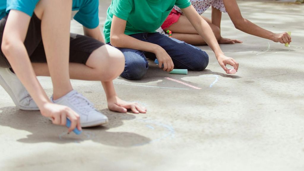 Niños pintando con tiza en un patio de un colegio